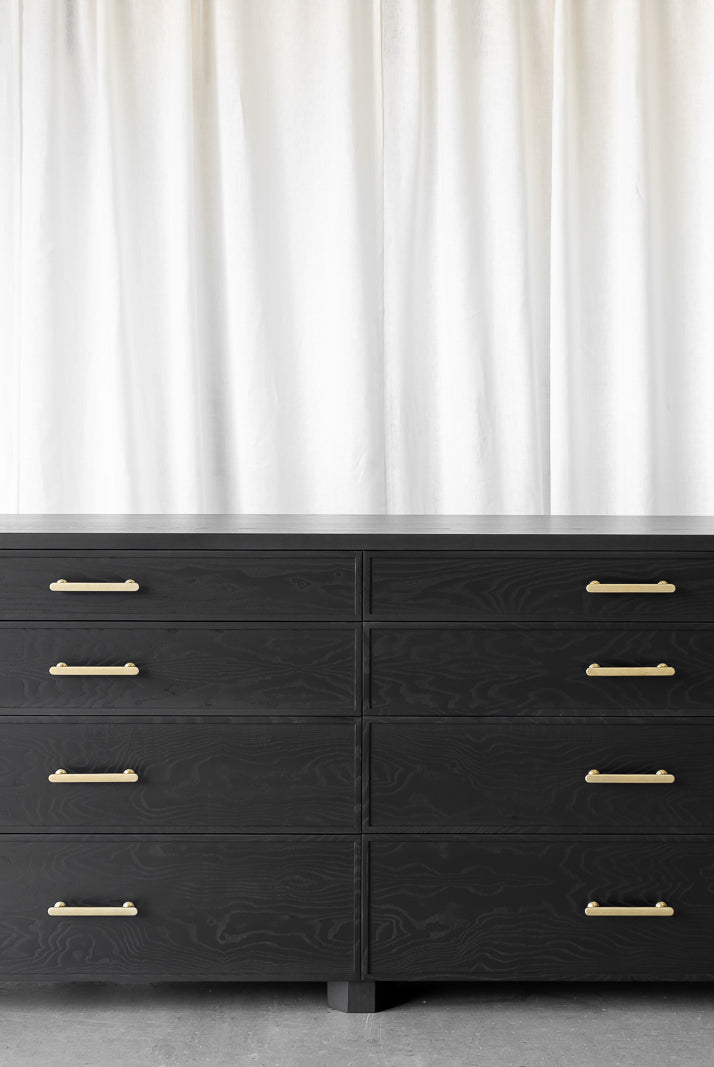 Black wooden sideboard, with visible wood grain. 8 drawers, antique brass handles and geometrical feet