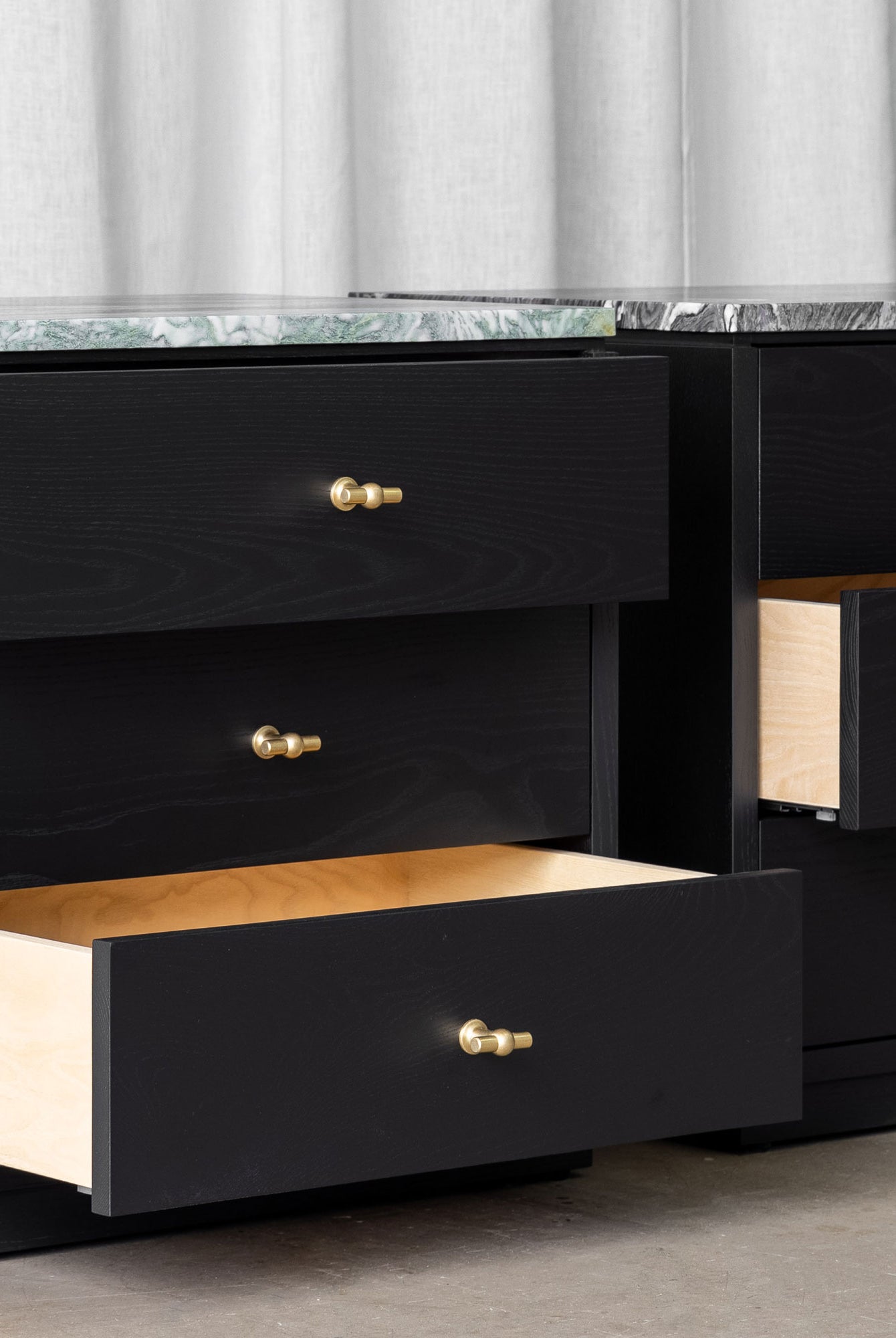 Pair of black wooden bedside cabinets with 3 drawers each, brass T-shaped handles and marble tops