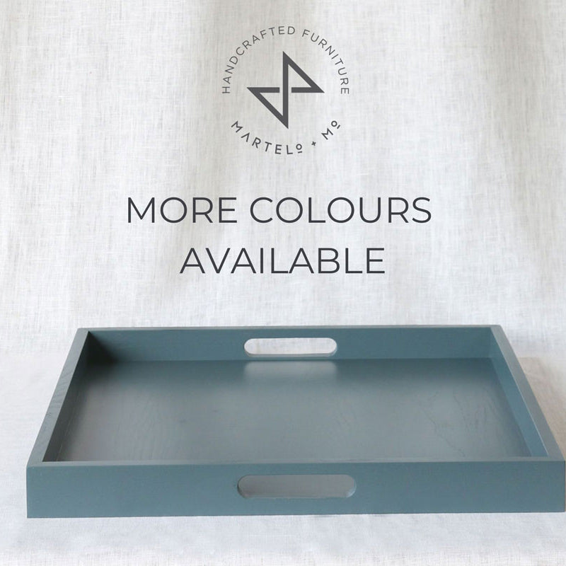 Blue-grey ottoman tray with cut-out handles and Martelo & Mo branding above, set against a light fabric backdrop with the text “More Colours Available.”