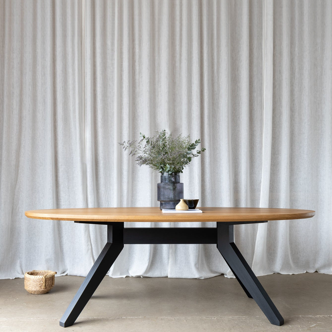 Image capturing the elegance of a styled 2.2-meter oval dining table, boasting a solid oak tabletop atop a sleek black base, timeless design and sophistication.