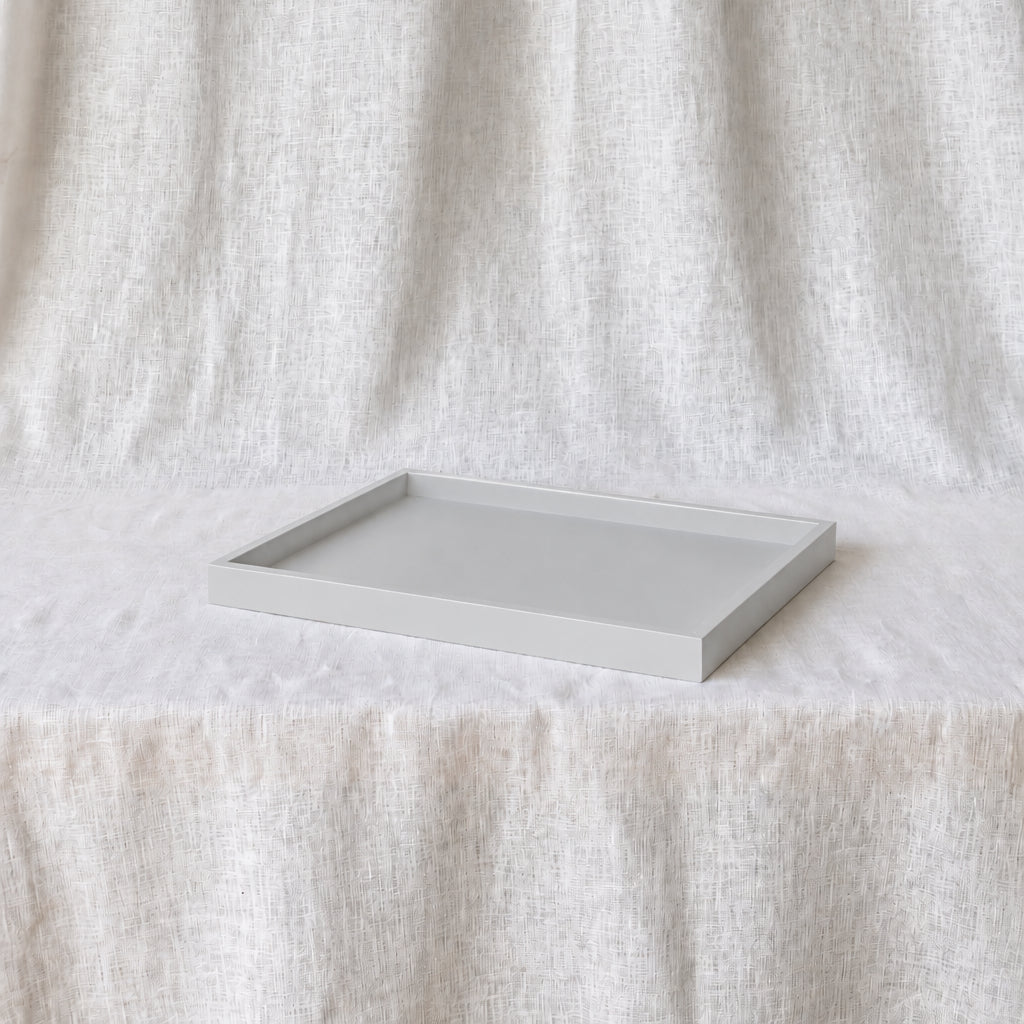 A minimalist rectangular tray with a light gray interior and a white exterior, resting on a textured white fabric surface against a matching draped fabric backdrop.