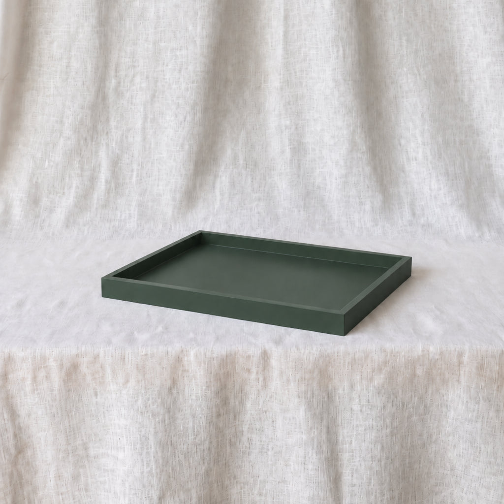 A dark green rectangular tray with a raised rim, displayed on a white textured fabric surface against a matching draped fabric backdrop.