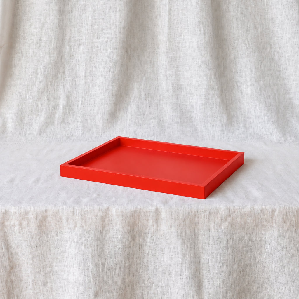 A bright red rectangular tray with raised edges, placed on a draped off-white fabric surface against a matching fabric backdrop.