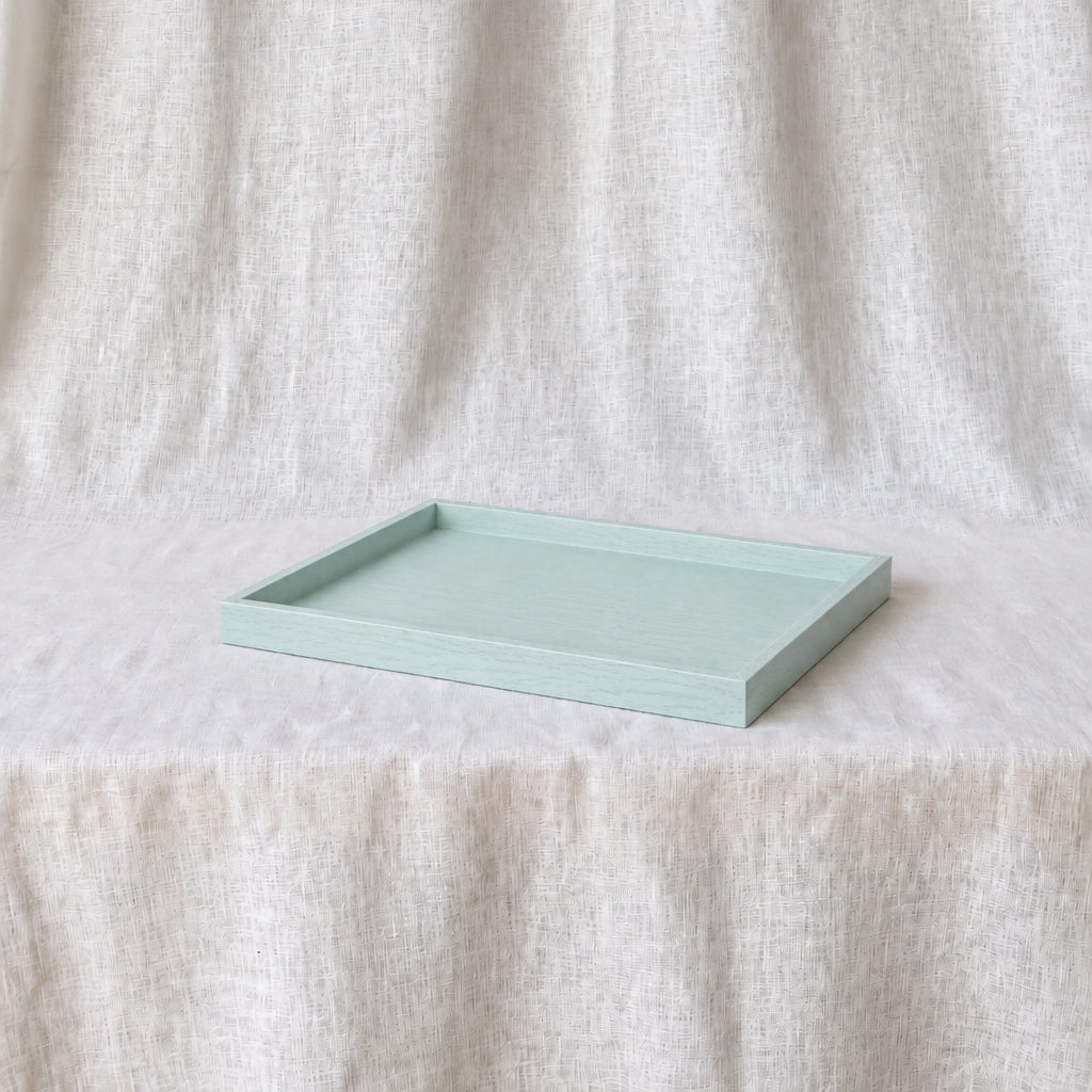A rectangular light blue tray with raised edges, resting on a draped cream linen fabric backdrop.