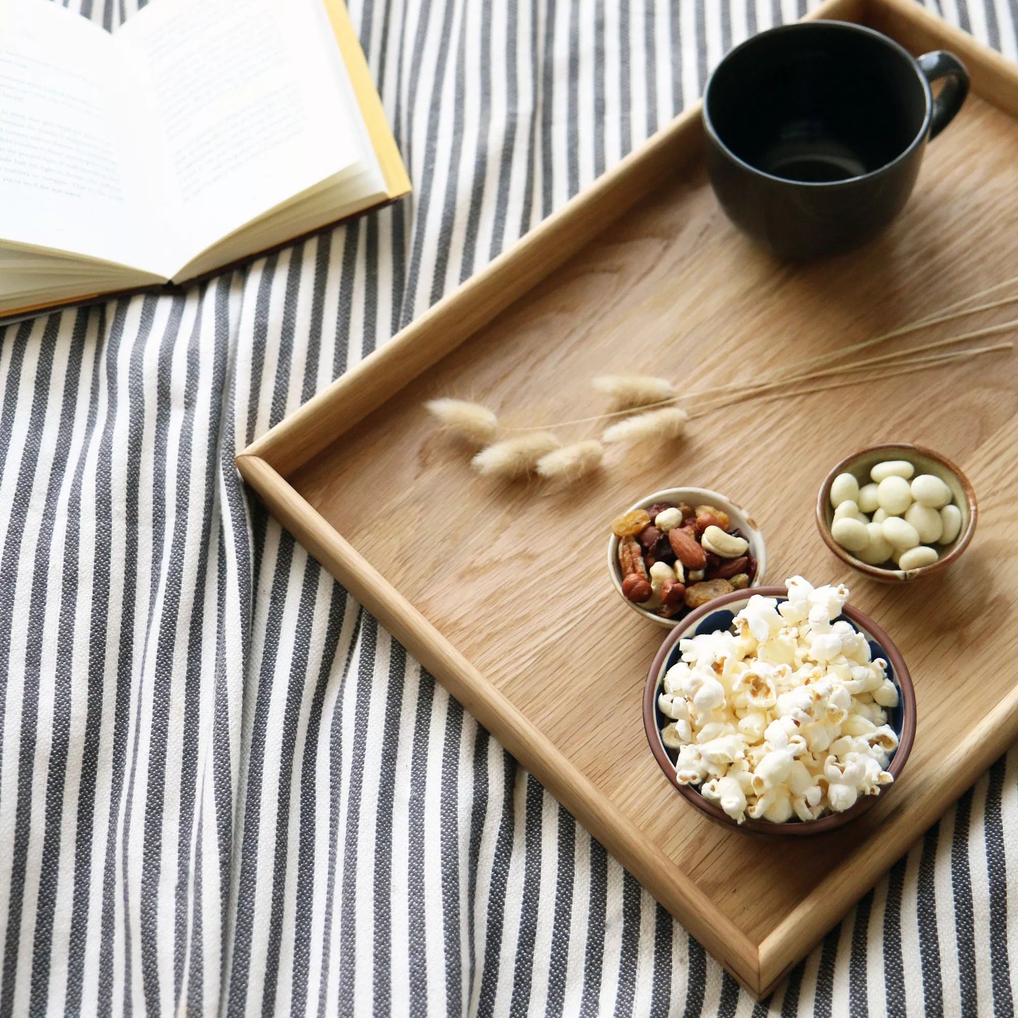 Wooden tray with bowls of snacks on a striped fabric background