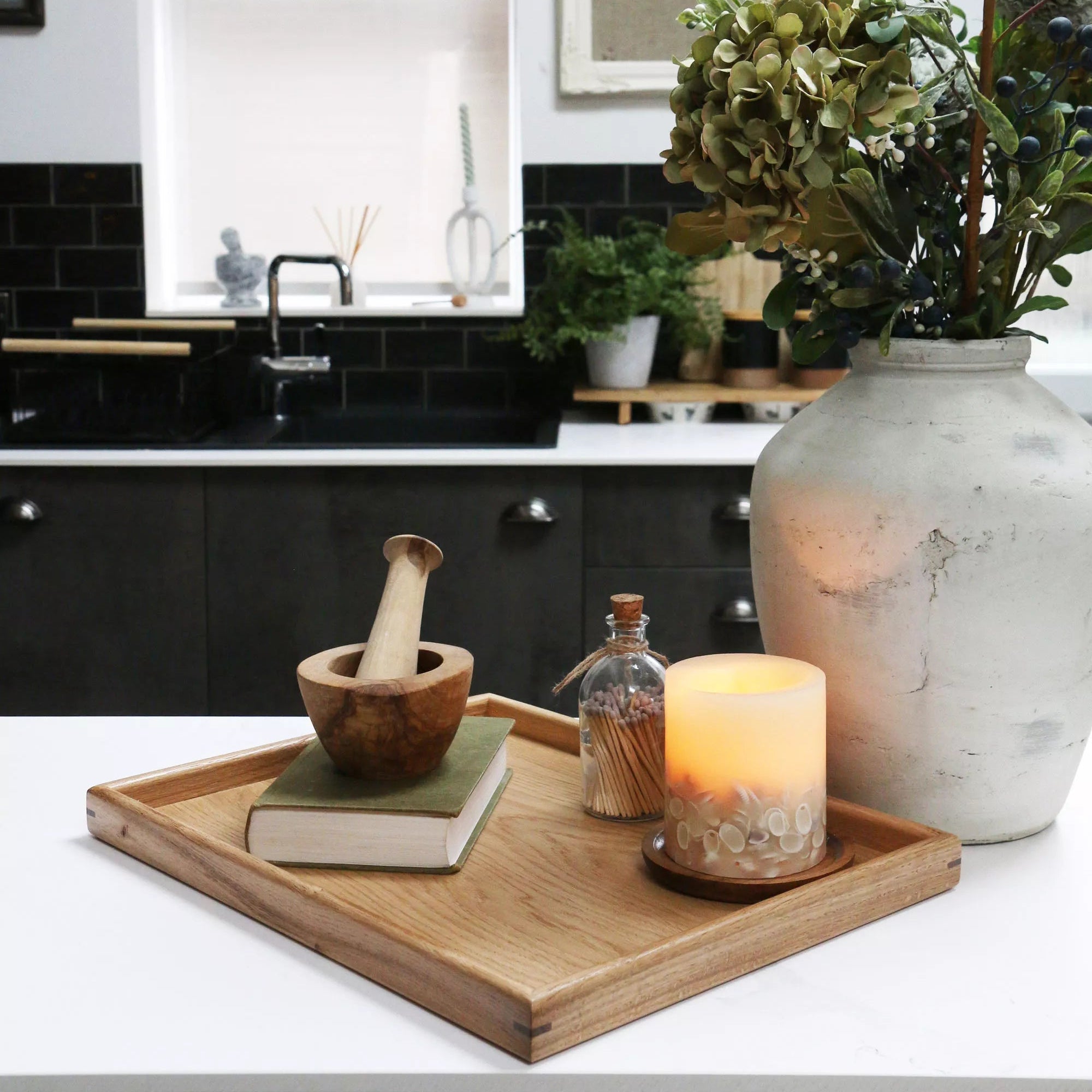 A decorative tray on a kitchen counter, styled with a candle, a book, and a wooden mortar and pestle, showcasing its versatility.