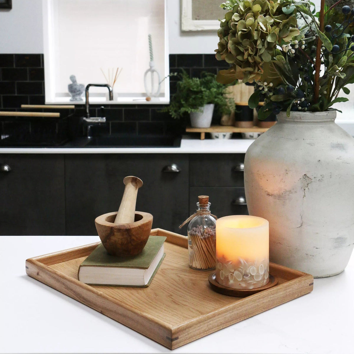 A decorative tray on a kitchen counter, styled with a candle, a book, and a wooden mortar and pestle, showcasing its versatility.
