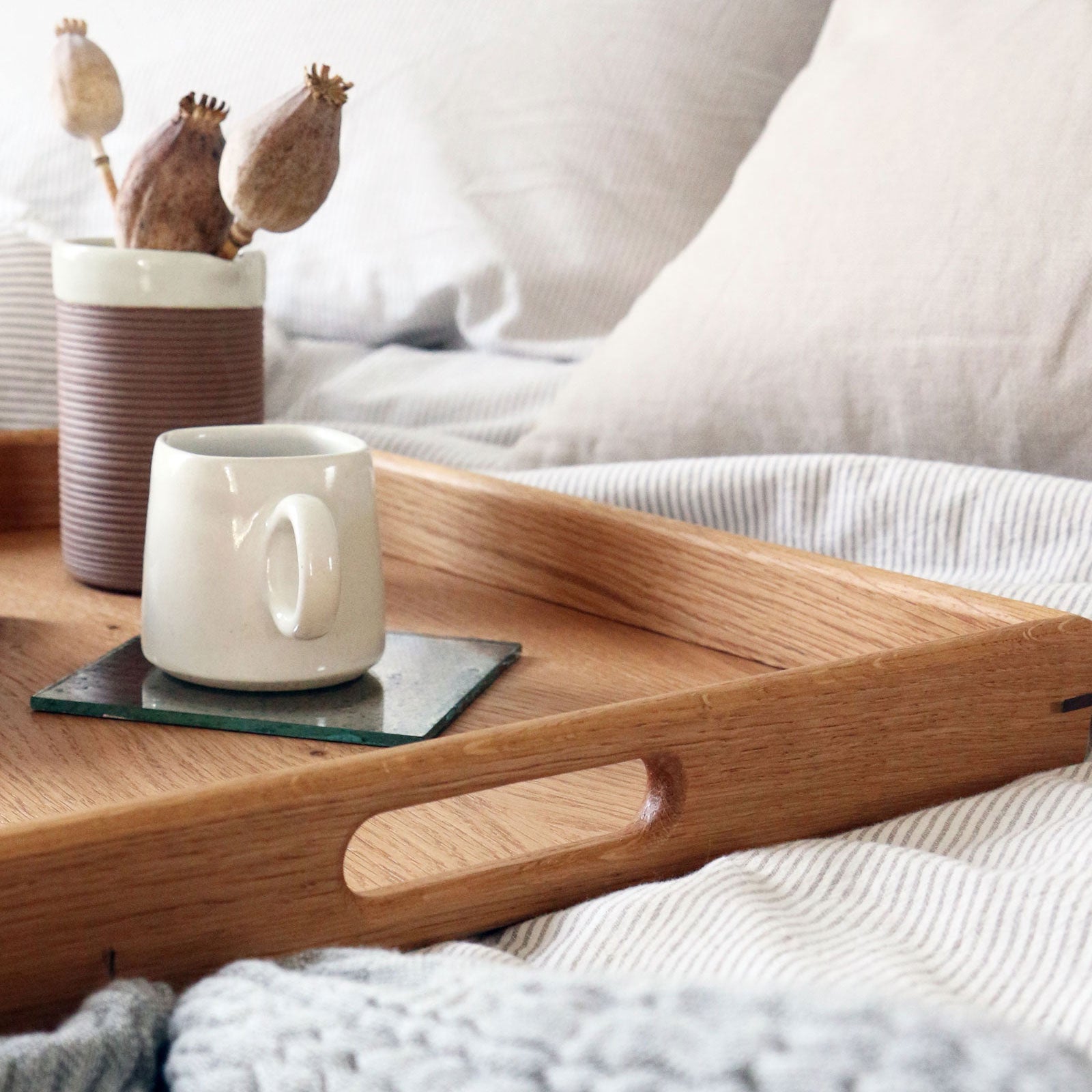 Side view of a large decorative tray with handles, elegantly styled on a bed with neutral linens and cozy textures.