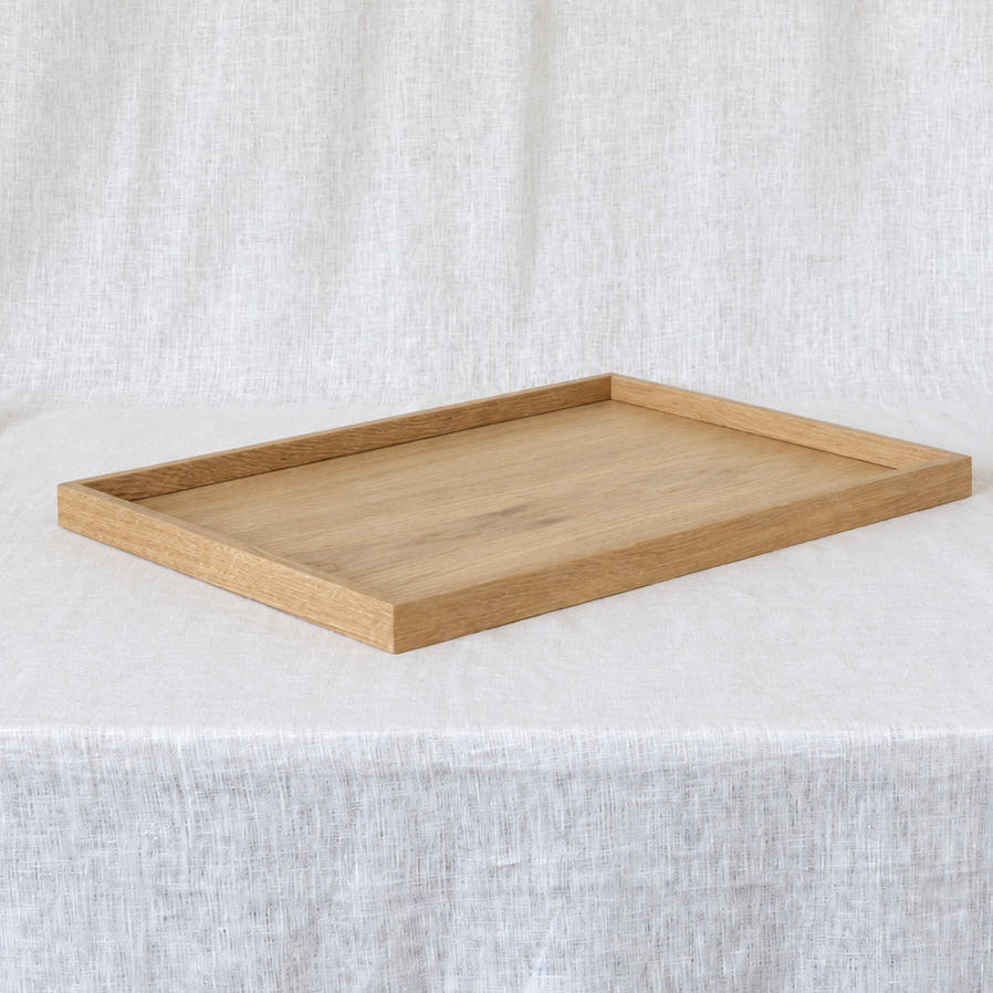 A rectangular wooden serving tray with a light oak finish, set on a draped white linen fabric background.