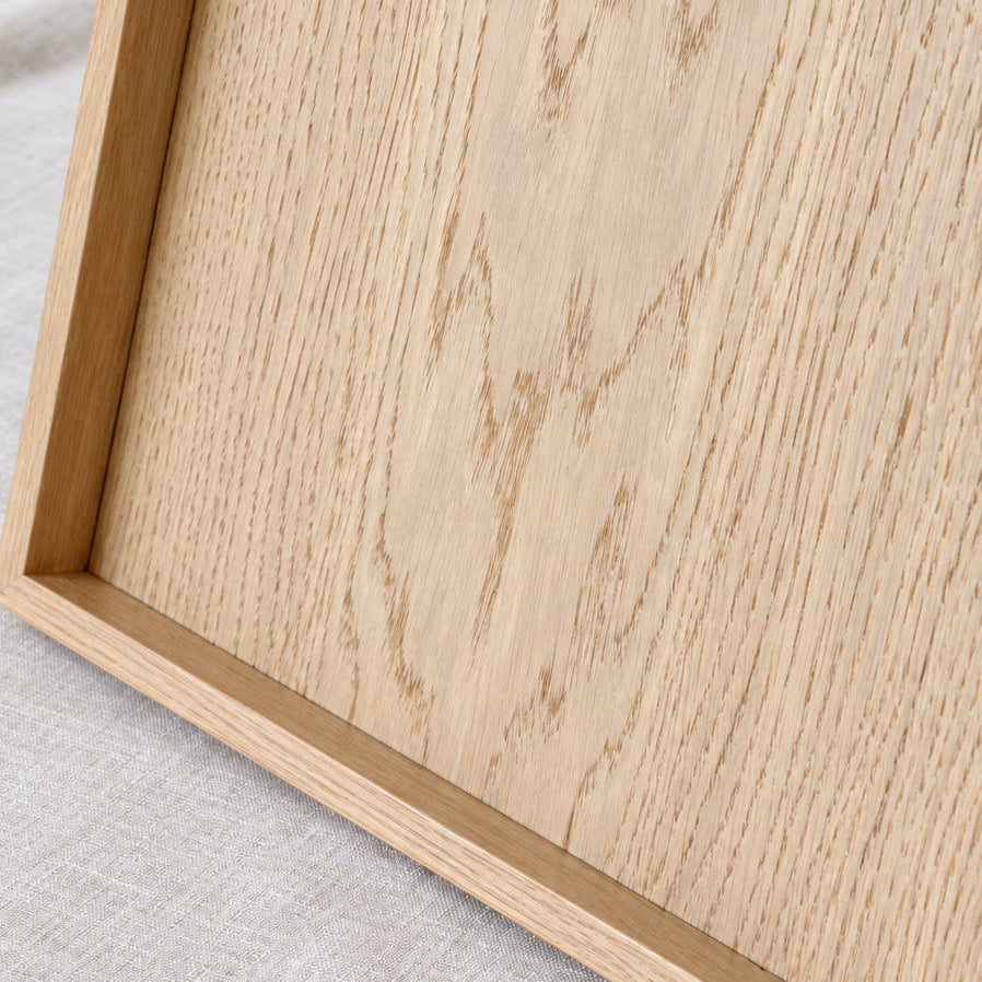 Close-up of a light natural oak wood serving tray resting on a textured light beige linen fabric background.