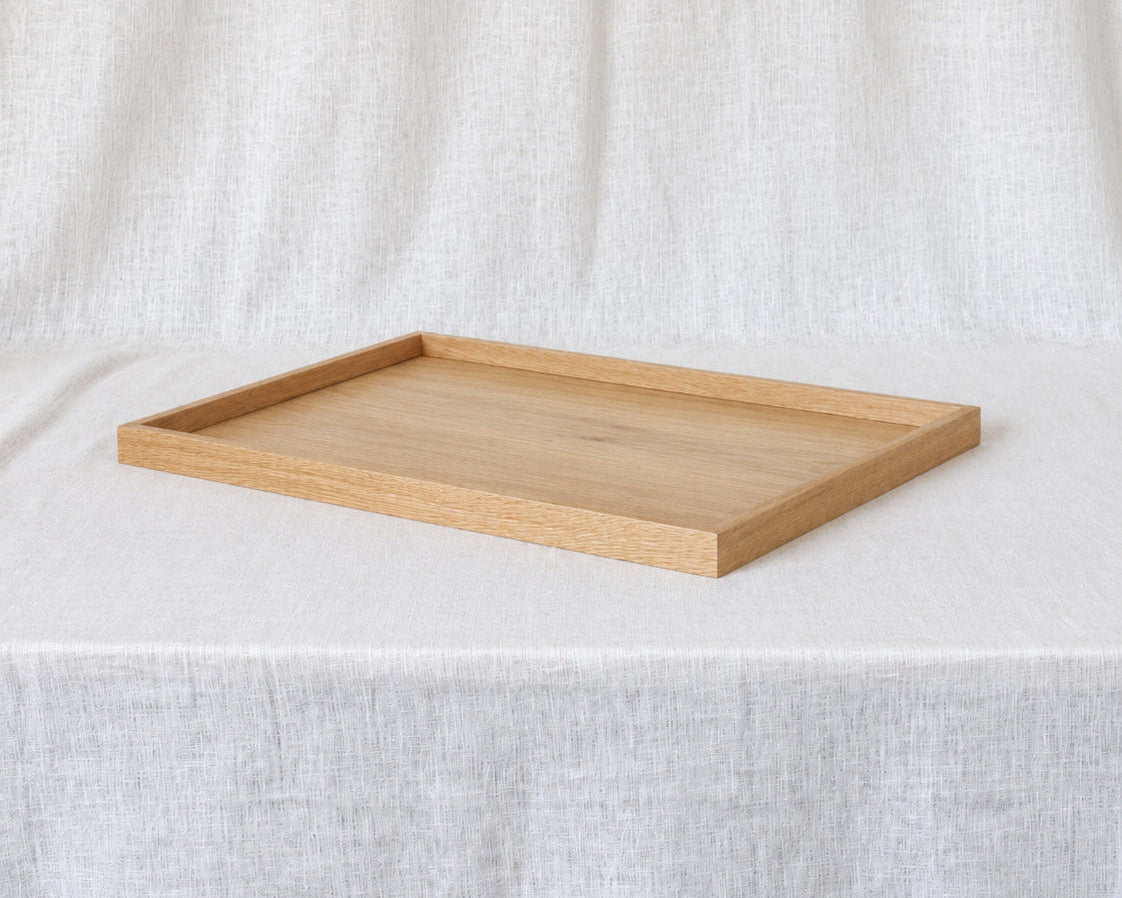 A rectangular light oak wooden tray with a raised rim, displayed on a draped white linen fabric background.