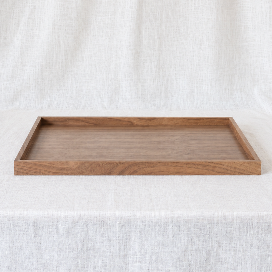 A rectangular wooden serving tray with a natural medium-brown finish and visible wood grain, displayed on a draped white linen fabric background.