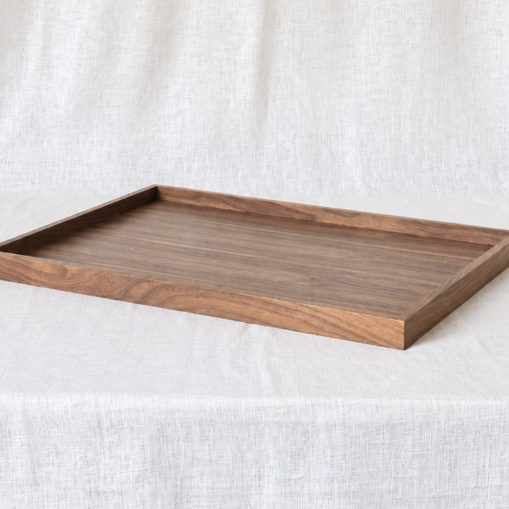 A rectangular wooden serving tray with a medium brown wood grain finish, displayed on a draped white linen fabric background.