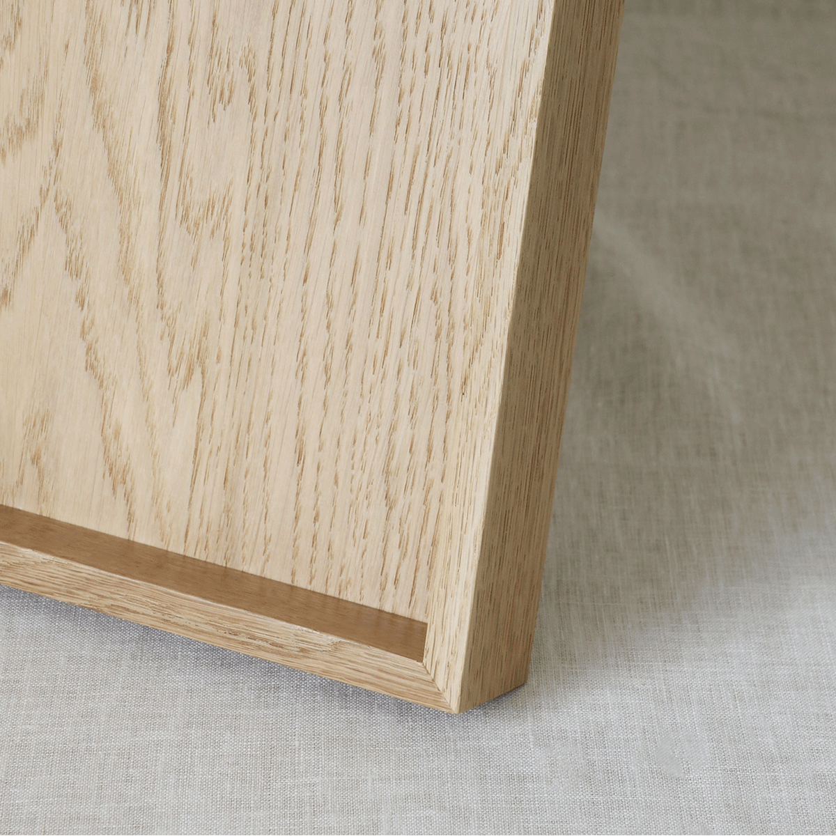 Close-up of a light natural wood tray corner resting on a textured off-white fabric surface.