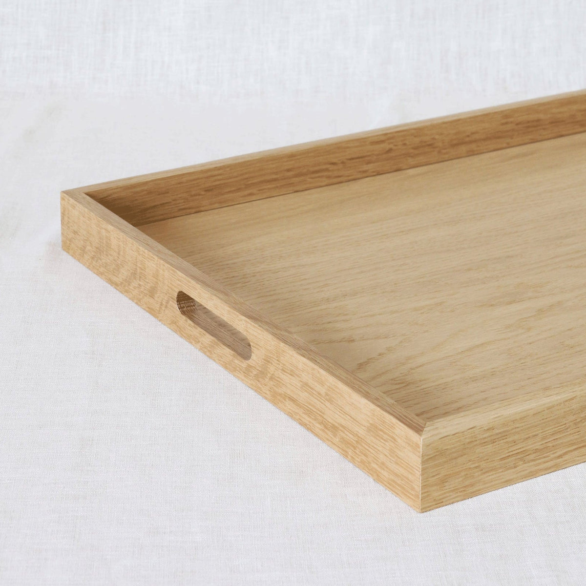 A light natural wood serving tray with a cutout handle, photographed on a white textured fabric background.