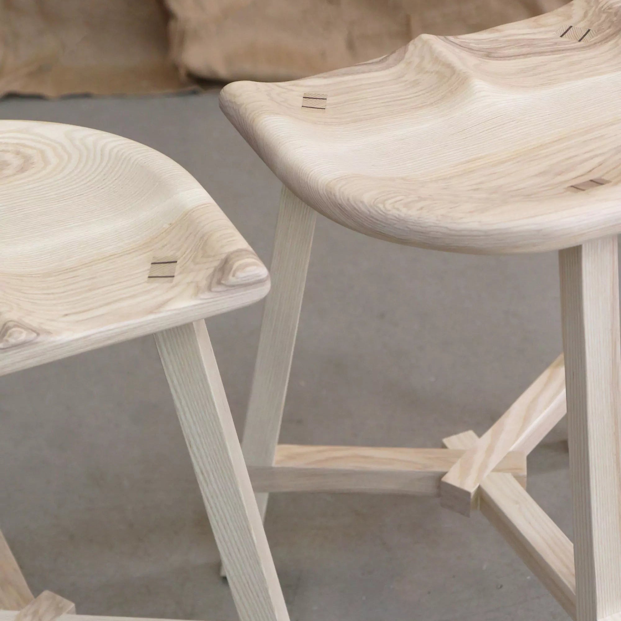 Two wooden stools with a natural finish on a gray floor.