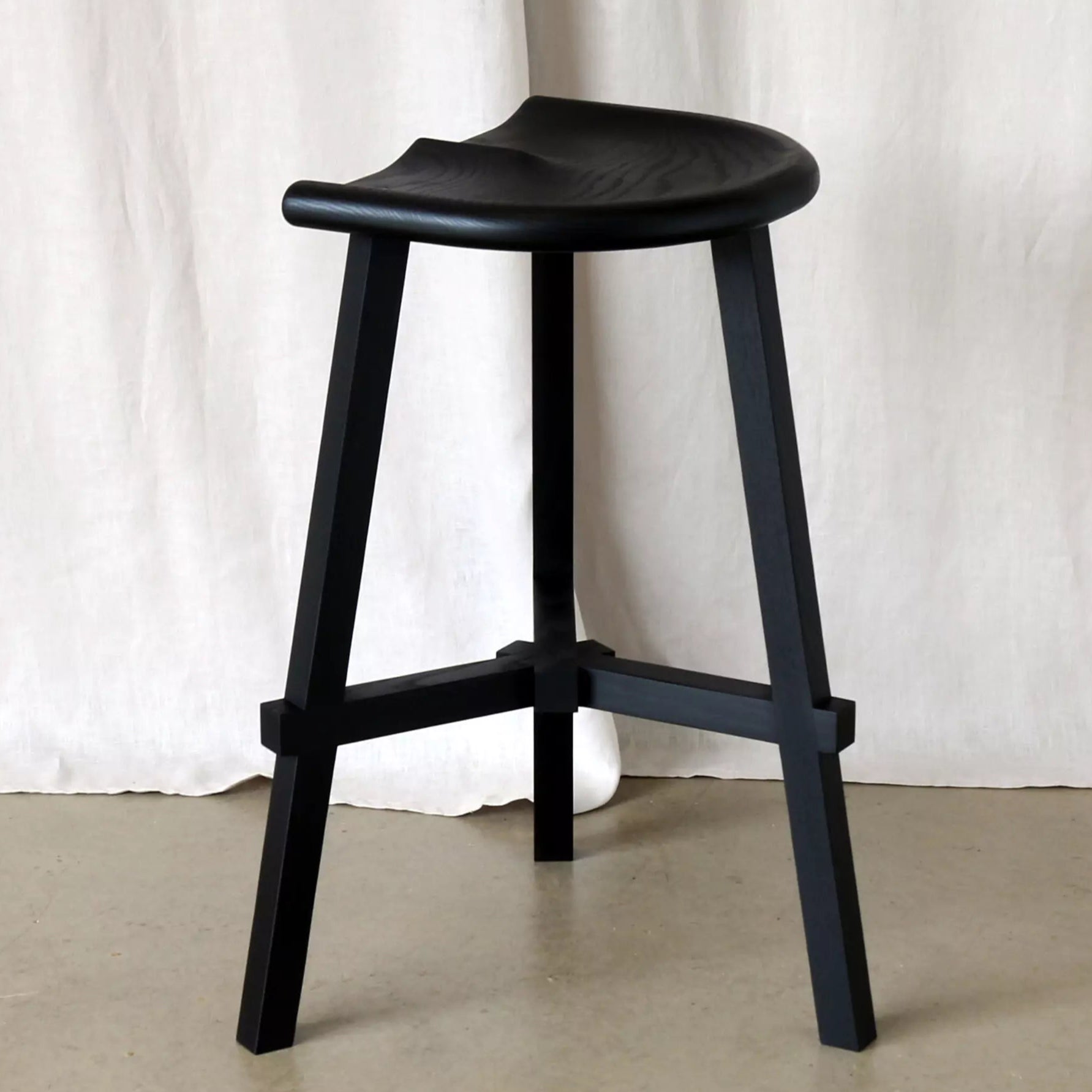 Black stool against a white curtain background