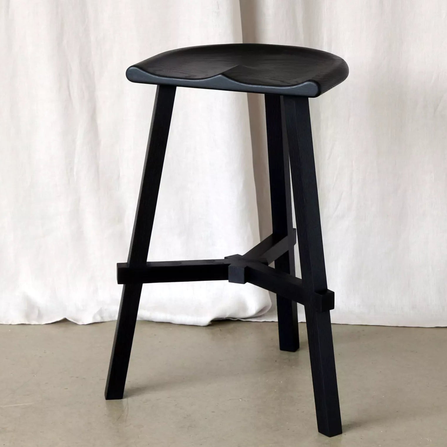 Black stool against a white curtain background