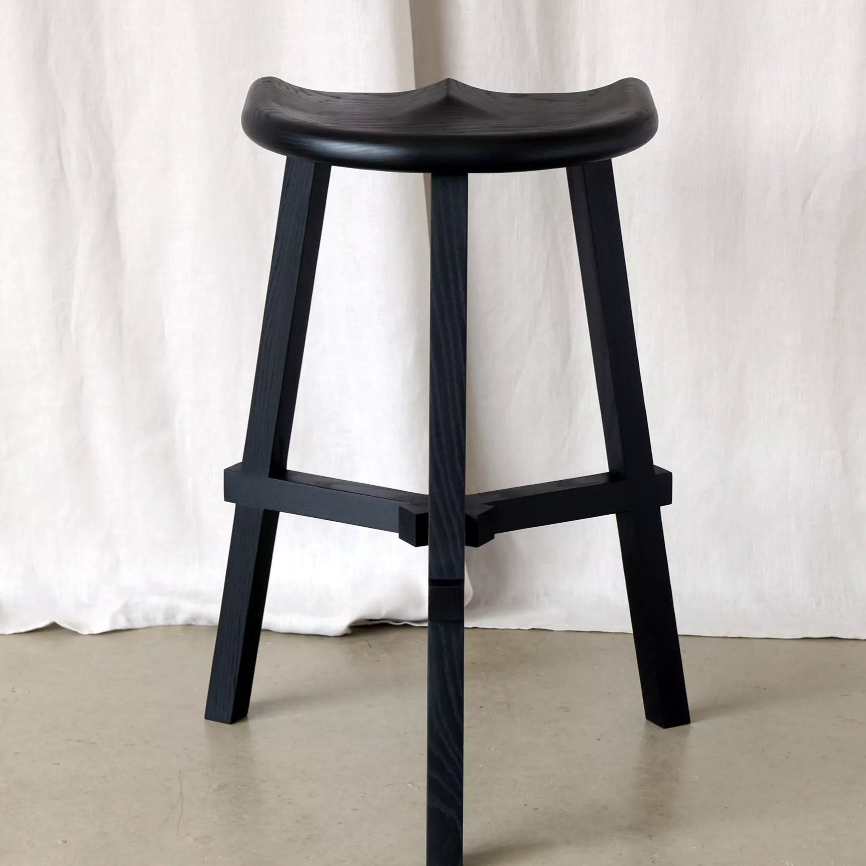 Black stool against a white curtain background