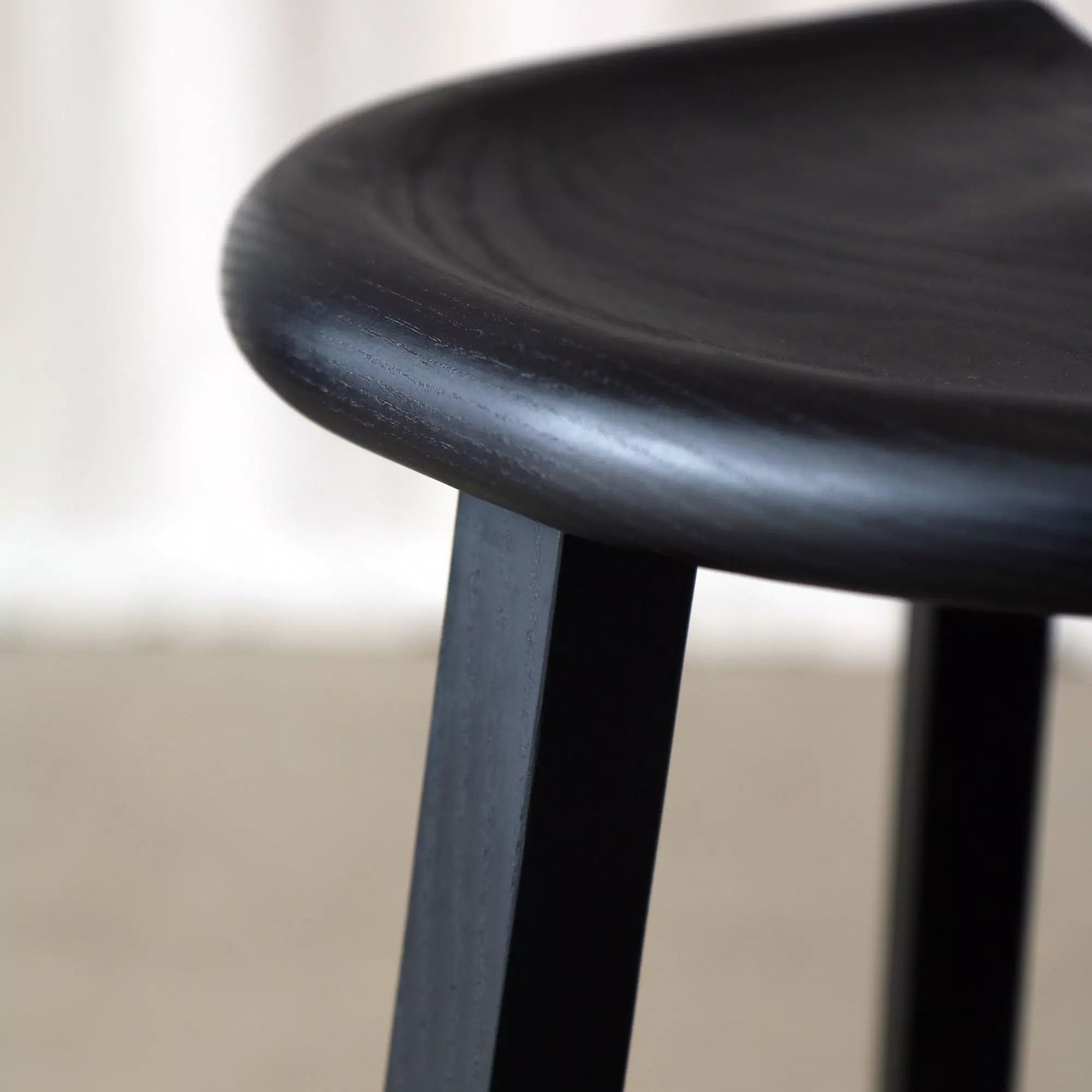 Close-up of a black stool with a carved seat and a  blurred background