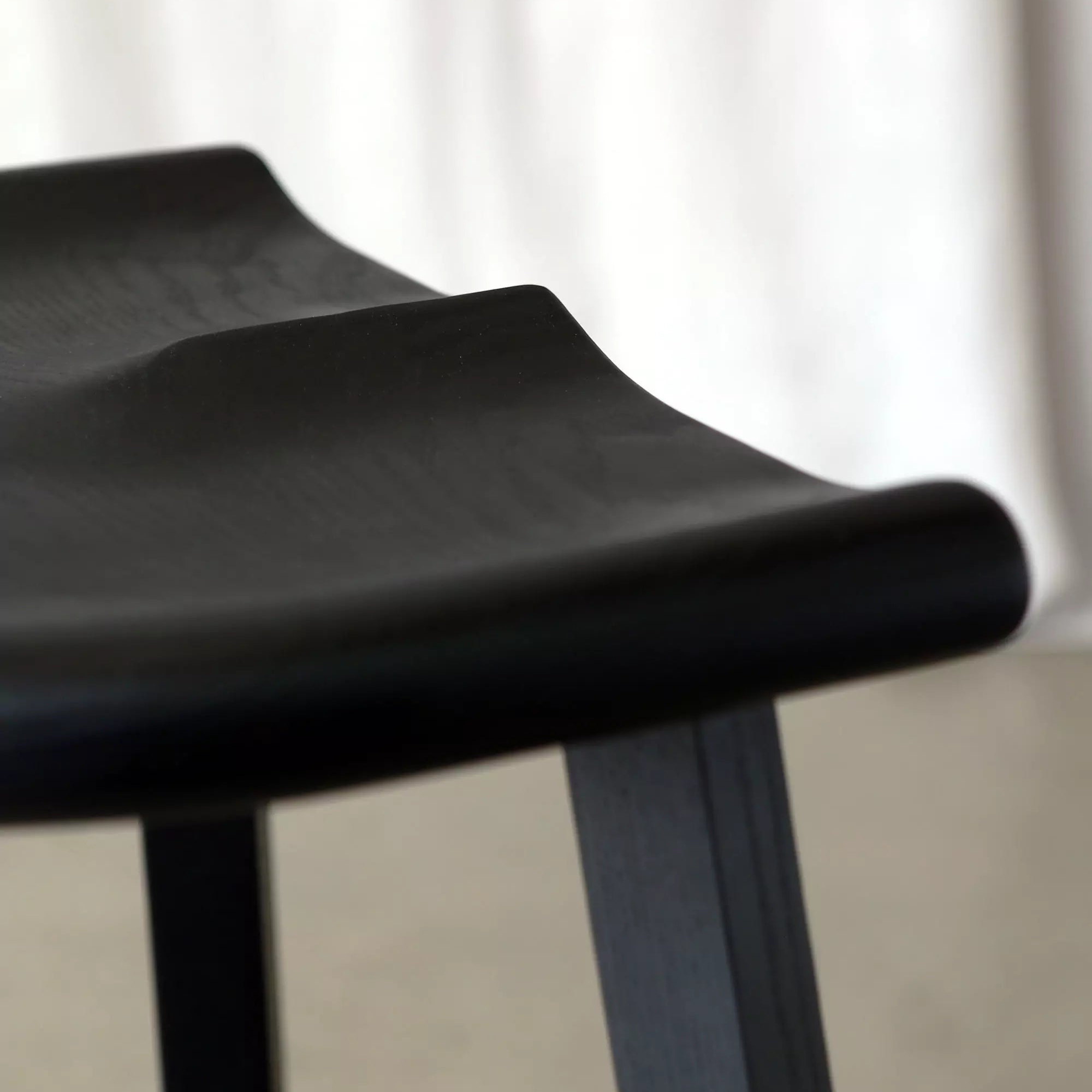 Black stool carved seat close-up with a blurred white curtain background