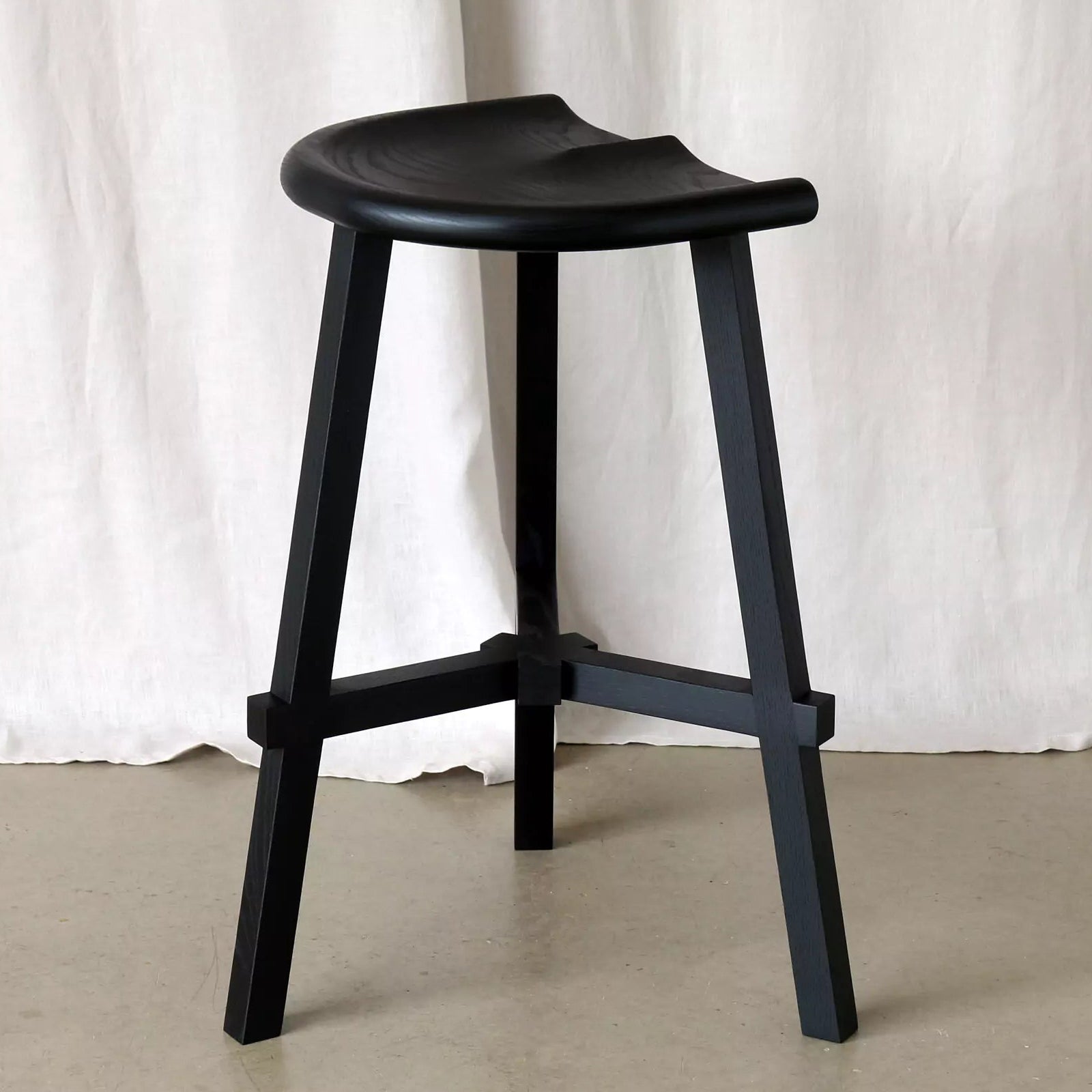 Black stool against a white curtain background