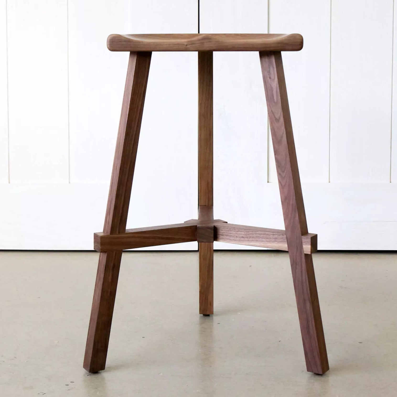 Wooden bar stool against a white paneled wall.