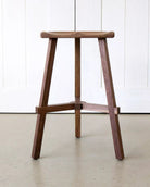 Wooden bar stool against a white paneled wall.