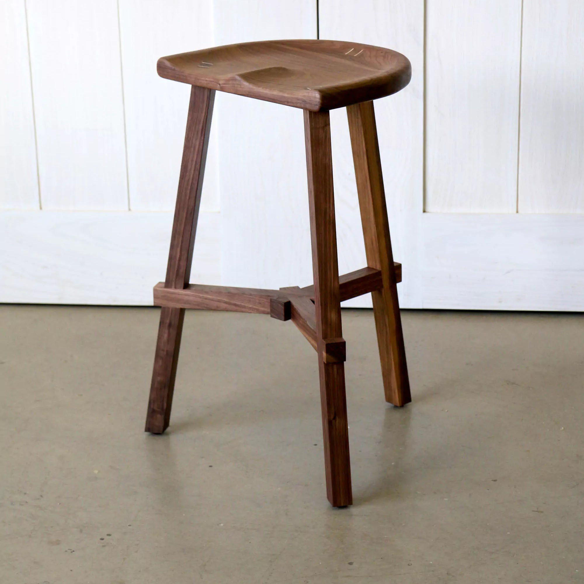 Walnut stool on a plain floor and white panelled wall background