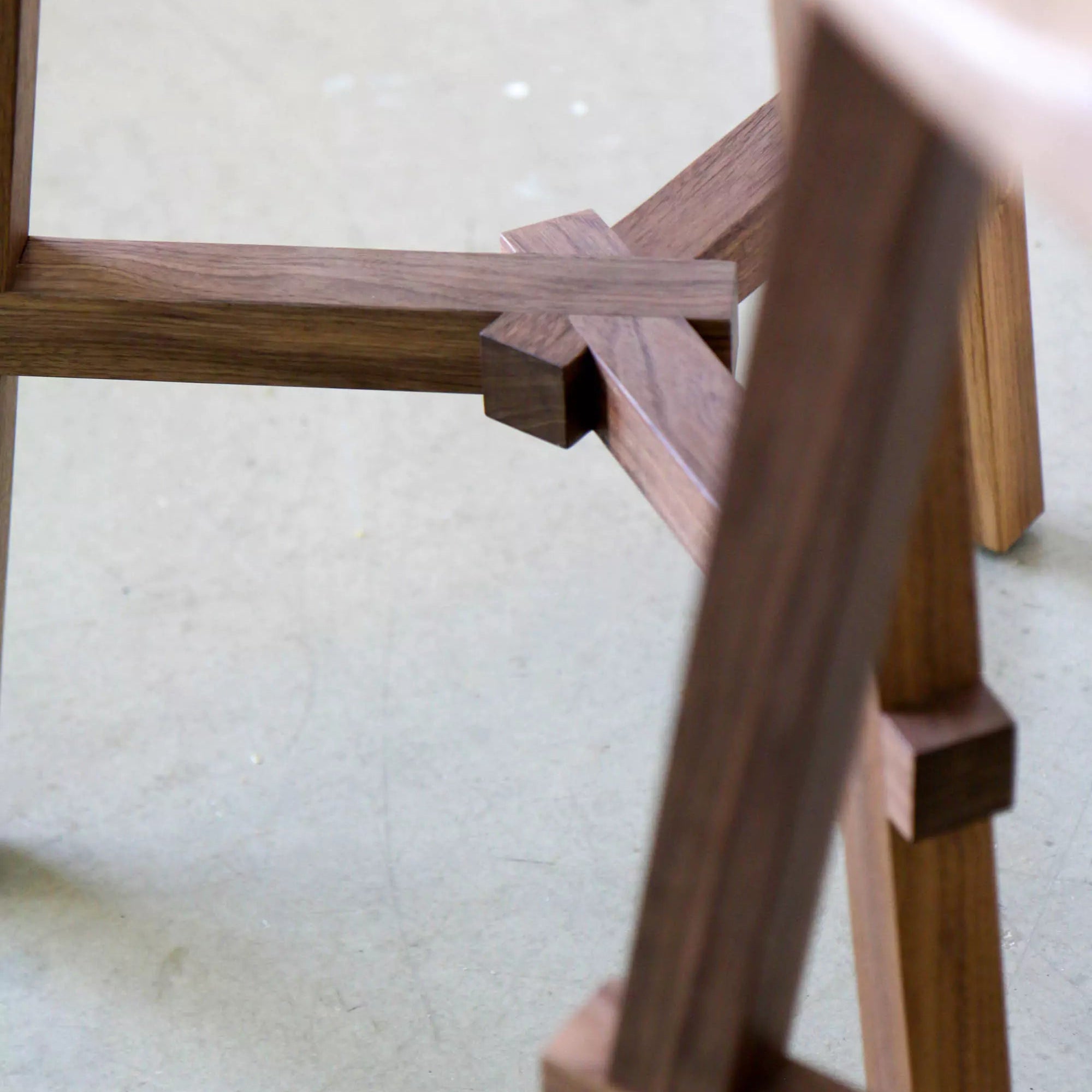 Close-up of a wooden stool frame on a light-colored floor.