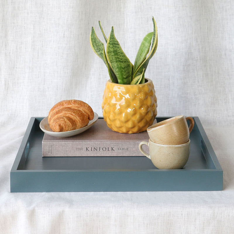 Styled tray with a yellow pineapple-pattern planter, stacked mugs, a croissant, and “The Kinfolk Table” book, with “More Colours Available” text and Martelo & Mo logo overlay.