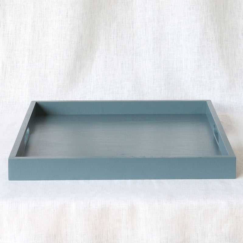 traight-on view of an empty blue-grey ottoman tray showing both handles, placed on a neutral fabric surface.