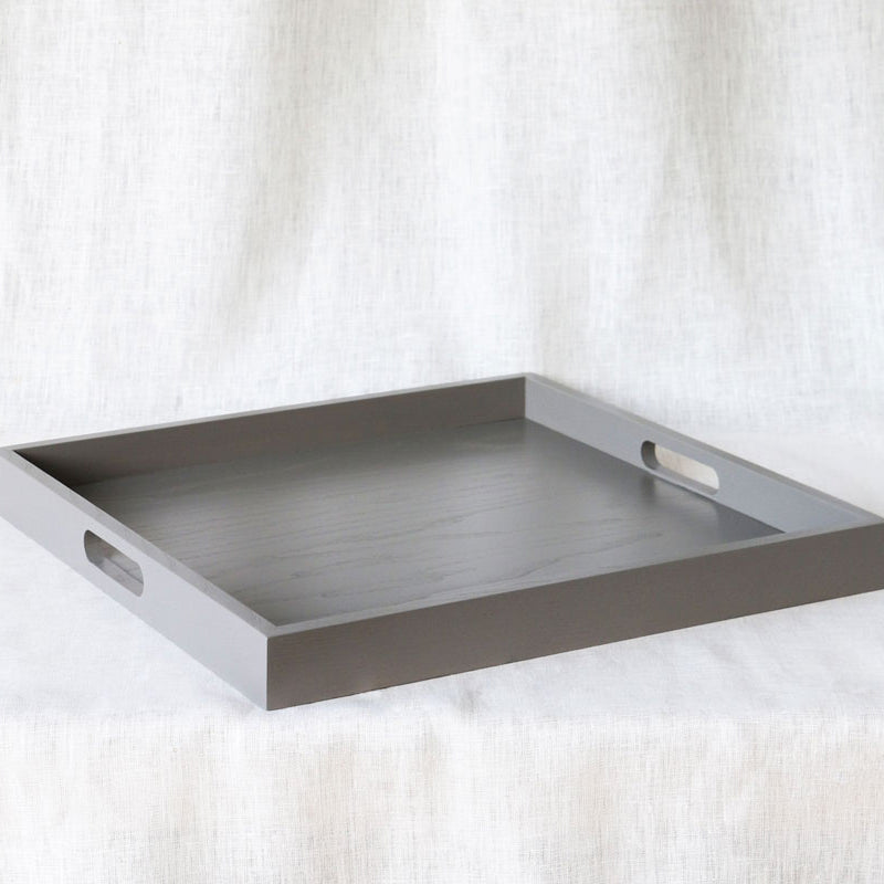 Side-angled view of a rectangular grey ottoman tray with both handles visible and wood texture slightly apparent.