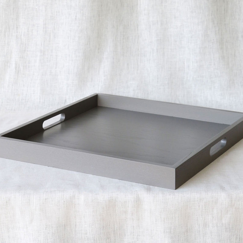 Wide-angle diagonal view of the grey ottoman tray with handles, placed on a soft fabric surface.