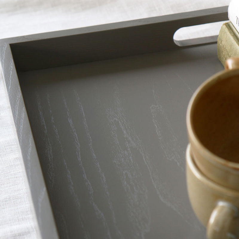 Angled view of the tray corner with visible wood grain and a ceramic cup partially shown in the frame.