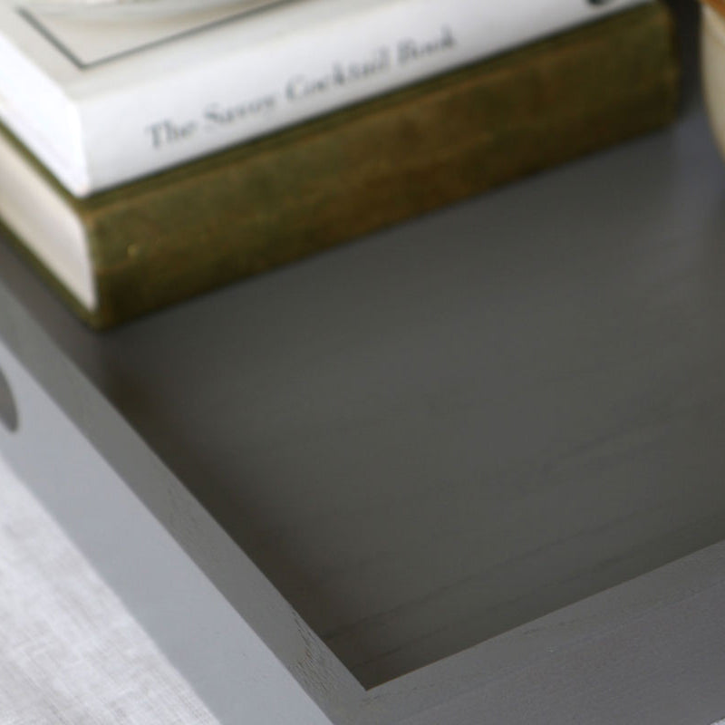 Close-up of a grey ottoman tray corner showing its smooth painted finish and subtle wood grain texture.