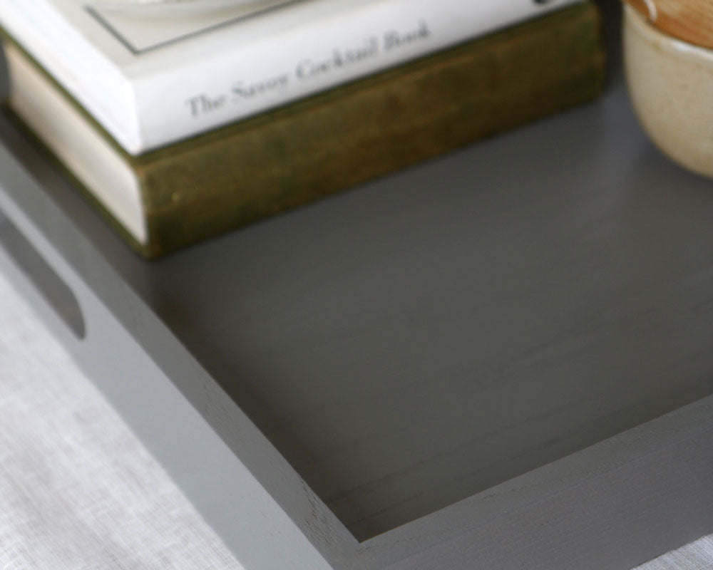 Close-up of a grey ottoman tray corner showing its smooth painted finish and subtle wood grain texture.