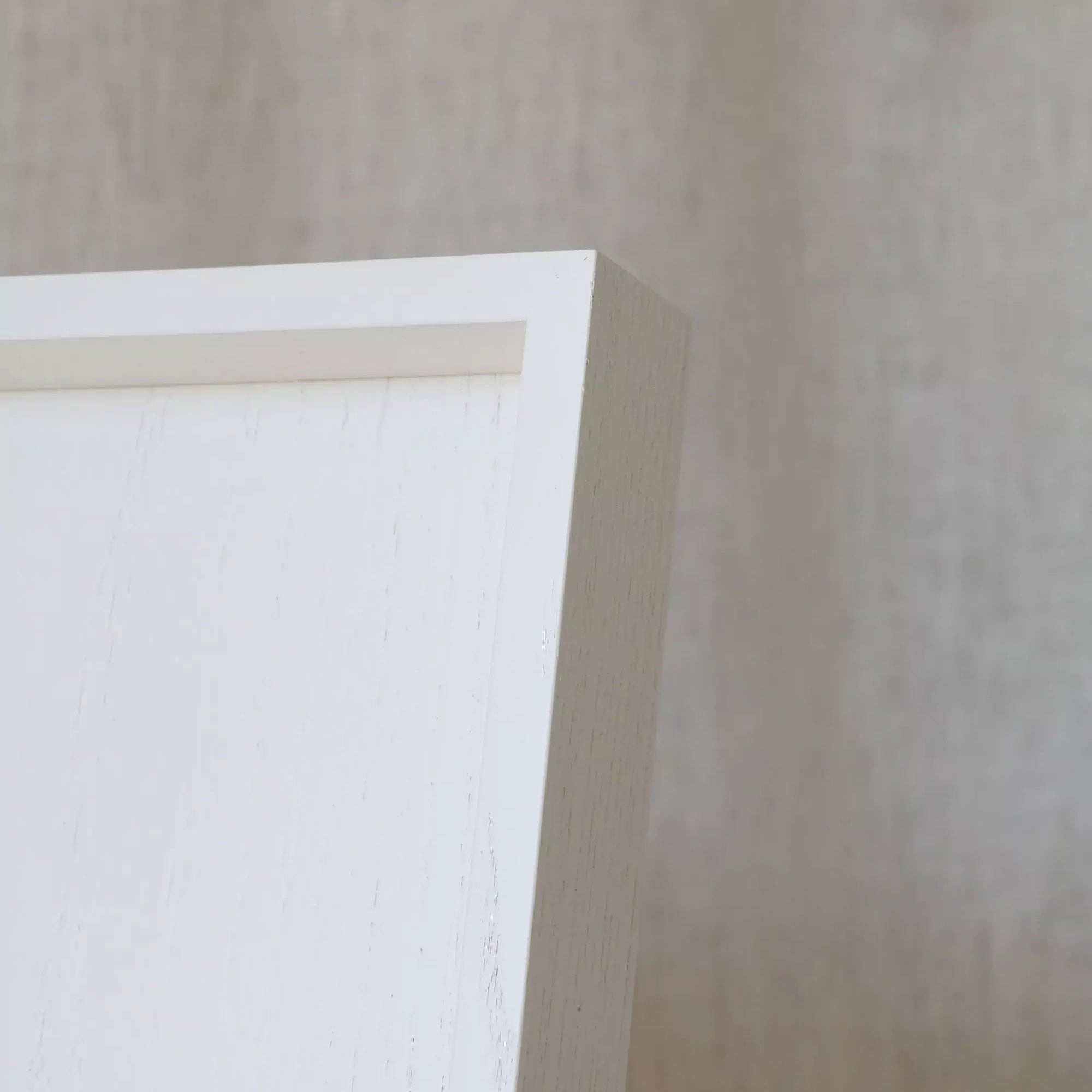 Close-up of a white ottoman tray frame corner on a beige wall.