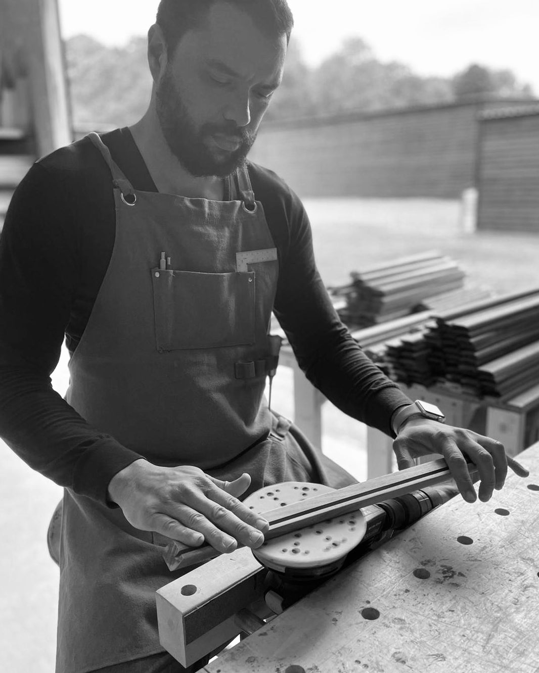 A skilled artisan sanding a wooden piece, wearing an apron, working in an open-air woodworking space, highlighting the craftsmanship behind handcrafted trays.
