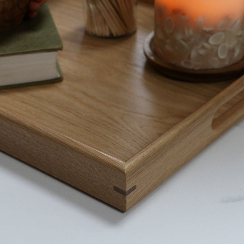 Detailed corner view of a wooden footstool tray, highlighting its smooth finish and precisely joined edges, accompanied by a candle and book.