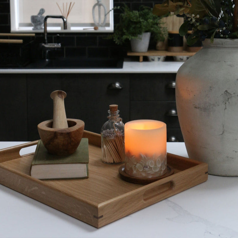 Handcrafted oak coffee table tray on a modern kitchen counter, decorated with a wooden mortar and pestle, a candle, and a glass jar of matches.