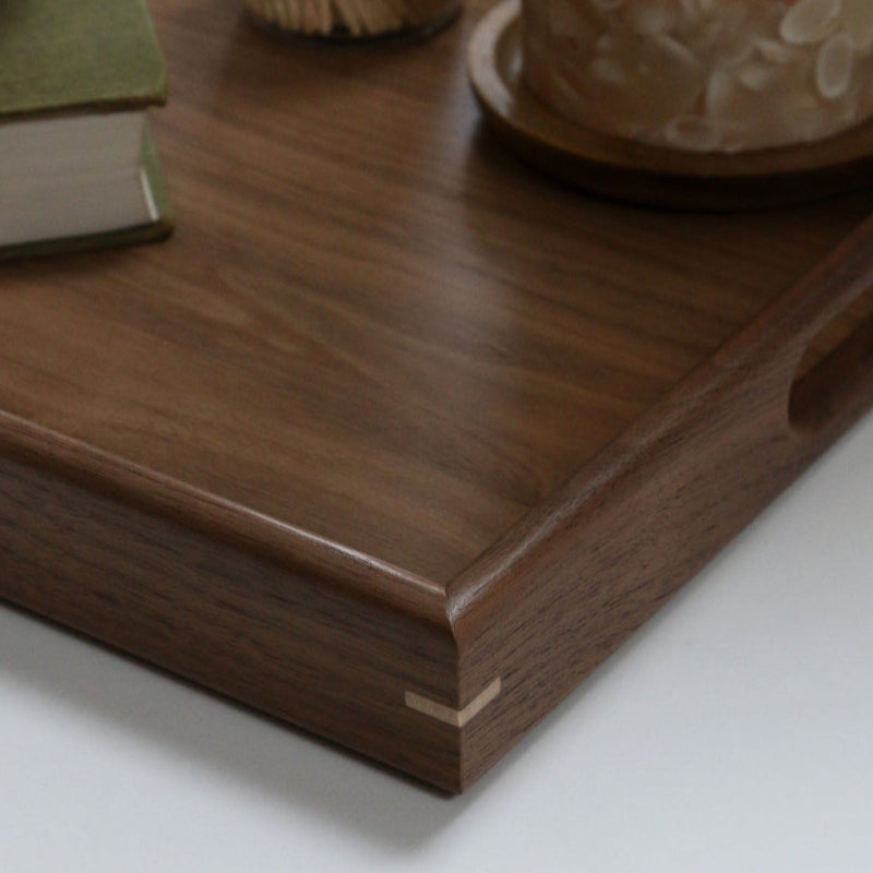 A handcrafted wooden tray styled in a modern kitchen with a mortar and pestle, a glowing candle, and rustic decor elements.
