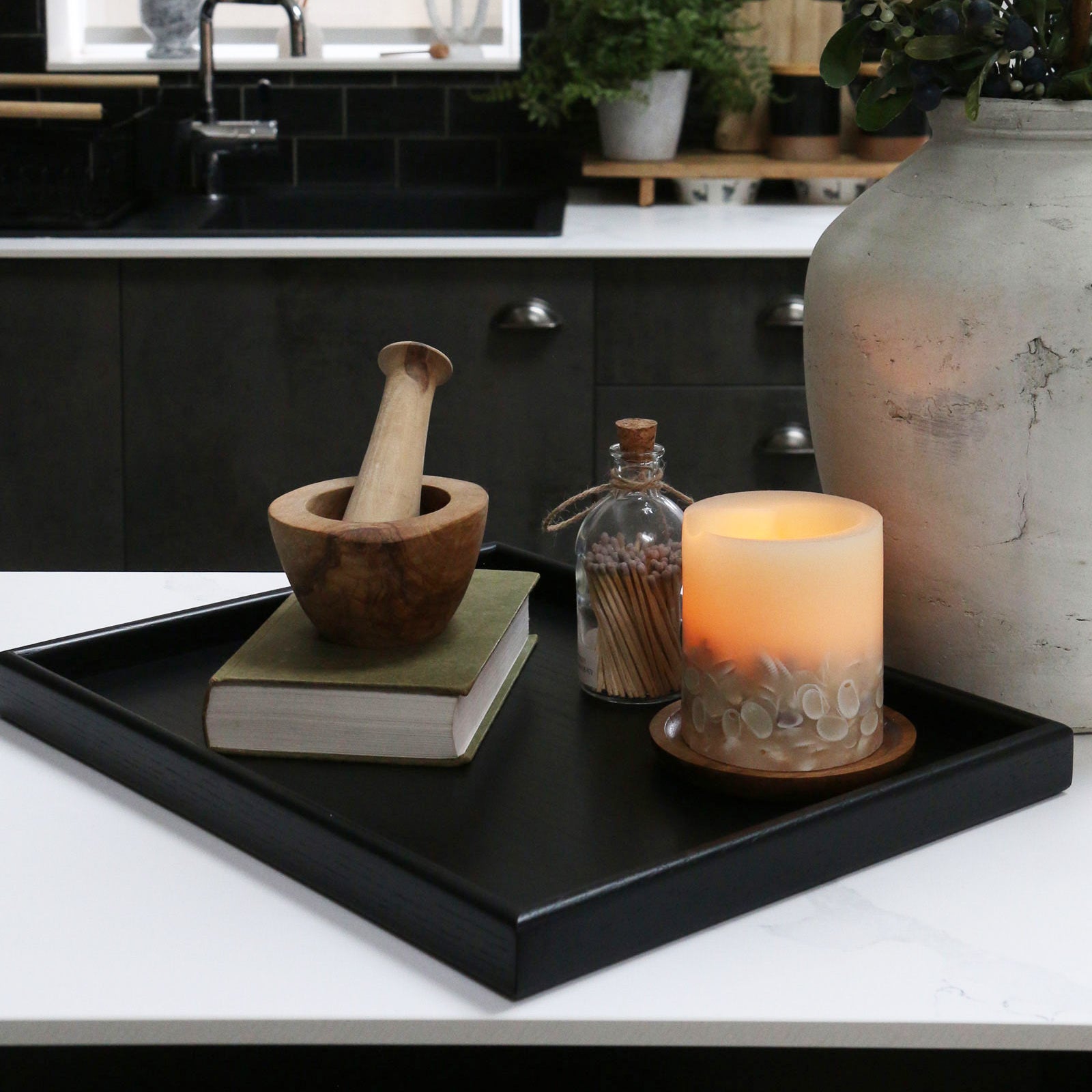 A decorative tray on a kitchen counter, styled with a candle, a book, and a wooden mortar and pestle, showcasing its versatility.