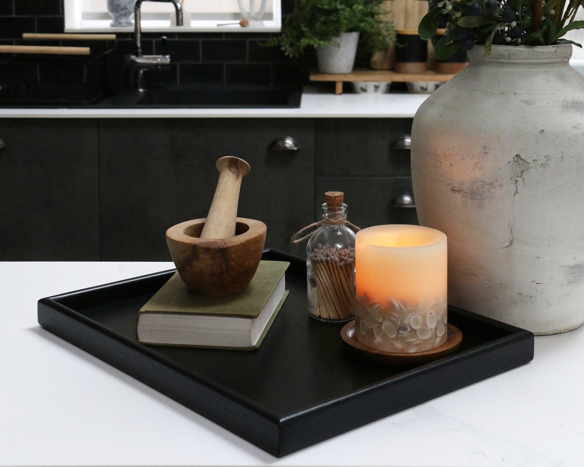 A decorative tray on a kitchen counter, styled with a candle, a book, and a wooden mortar and pestle, showcasing its versatility.