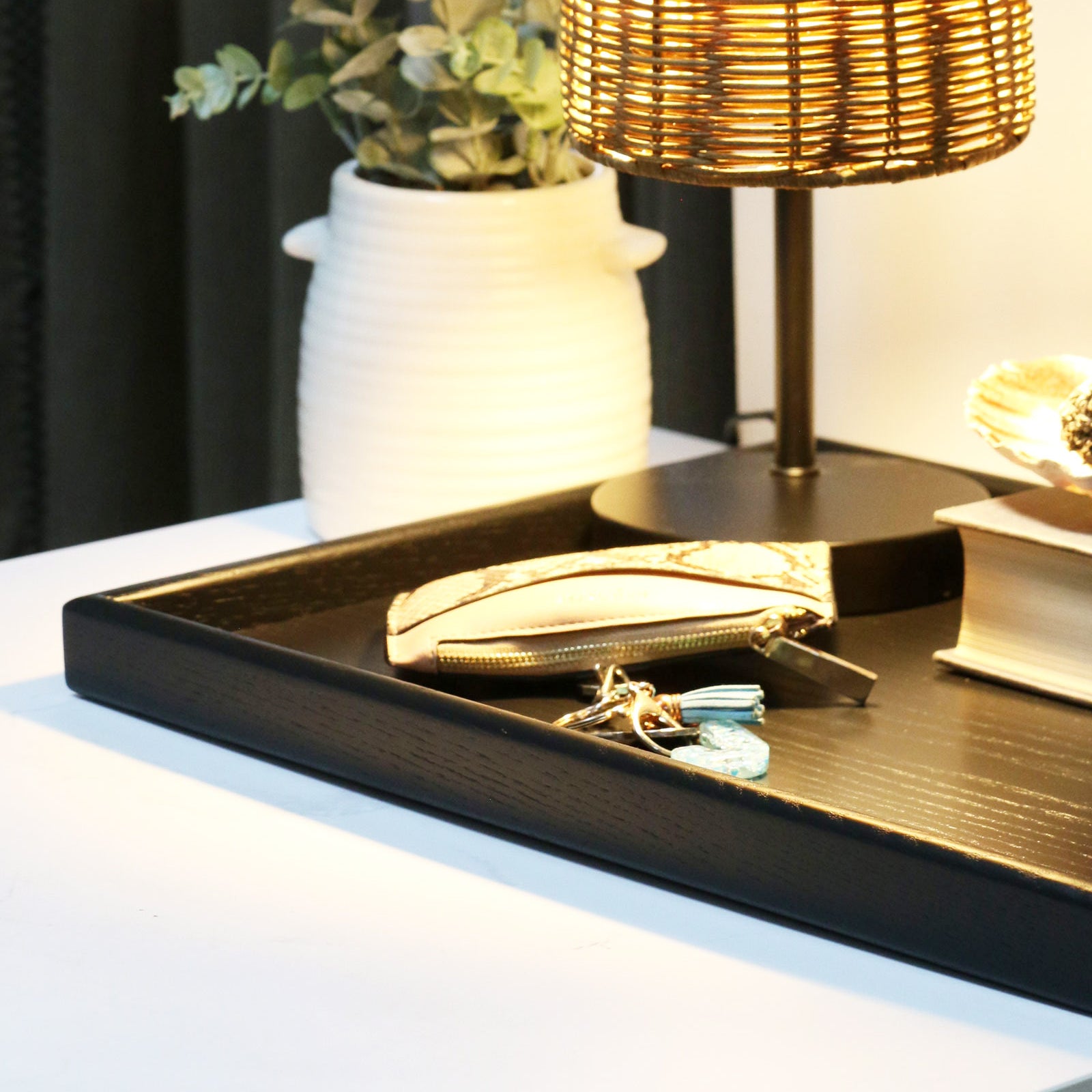 A decorative tray used as a stylish nightstand organizer, holding books, keys, and a lamp in a warm, ambient setting.
