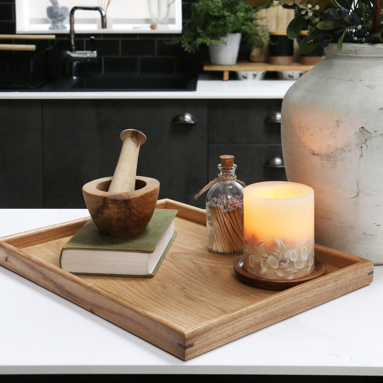 A decorative tray on a kitchen counter, styled with a candle, a book, and a wooden mortar and pestle, showcasing its versatility.