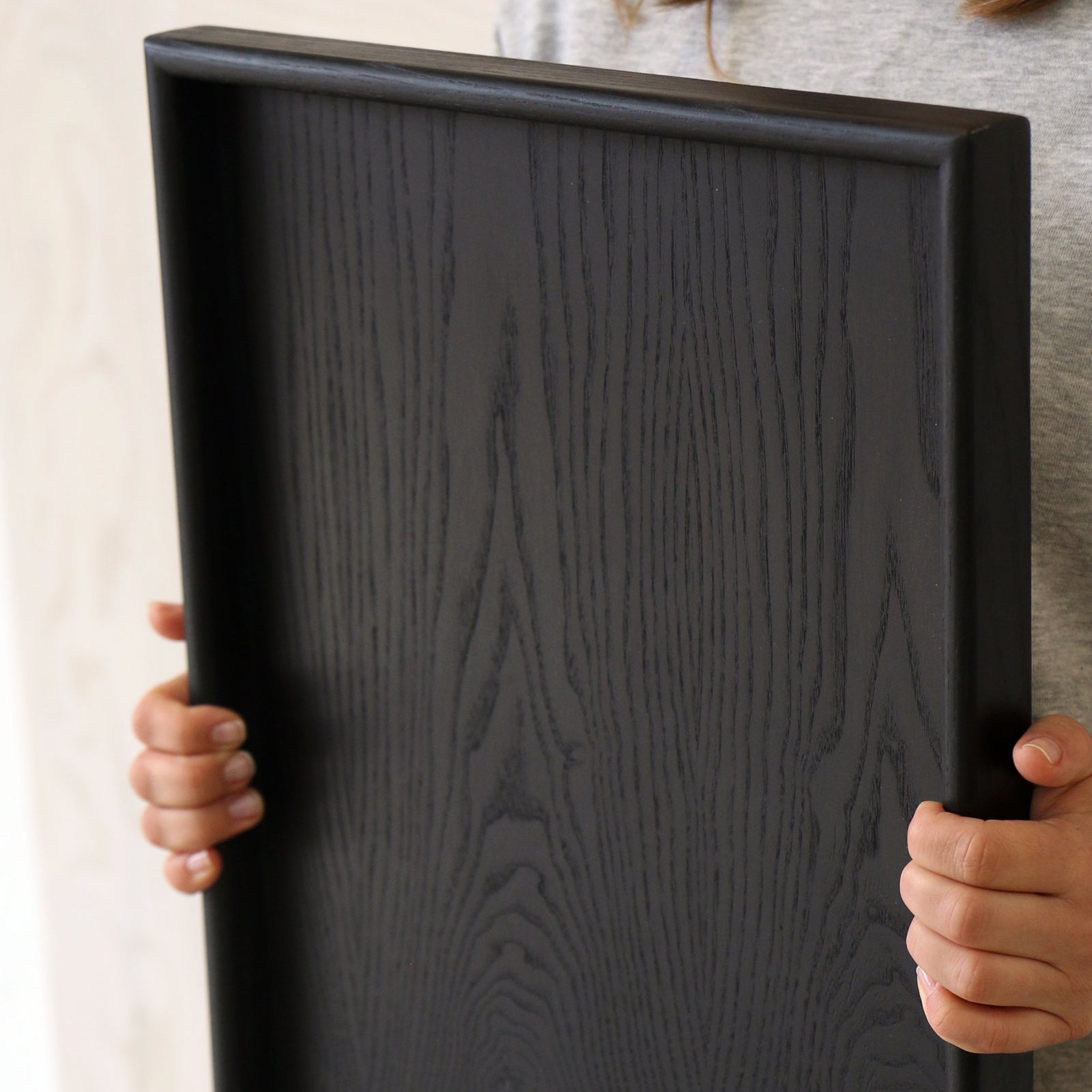 A wooden tray for footstool in use, being held to display its size and craftsmanship.