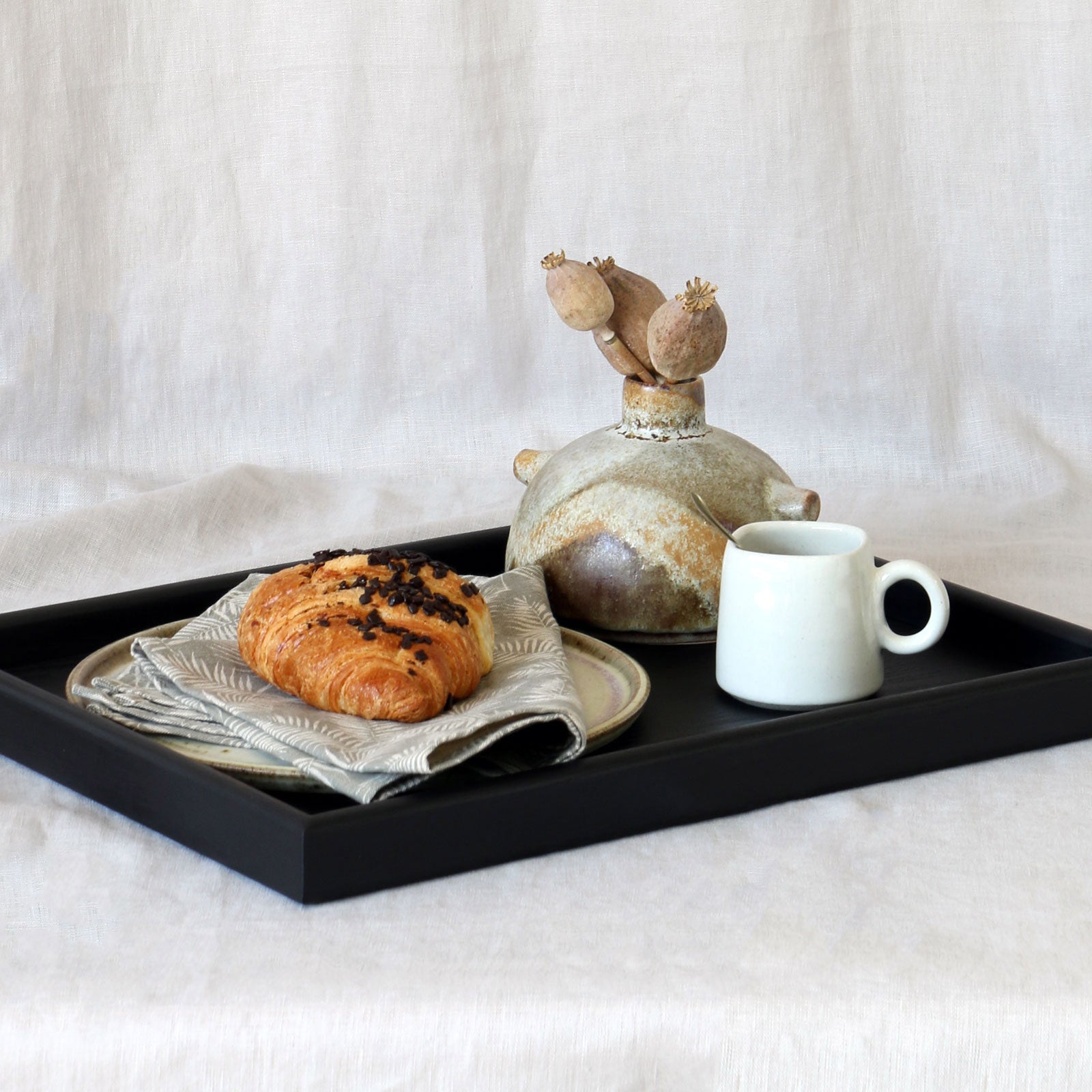 Coffee table tray in black wood, artistically arranged with a ceramic vase, cup, and napkin, showcasing its versatility as a decorative accent for living spaces.