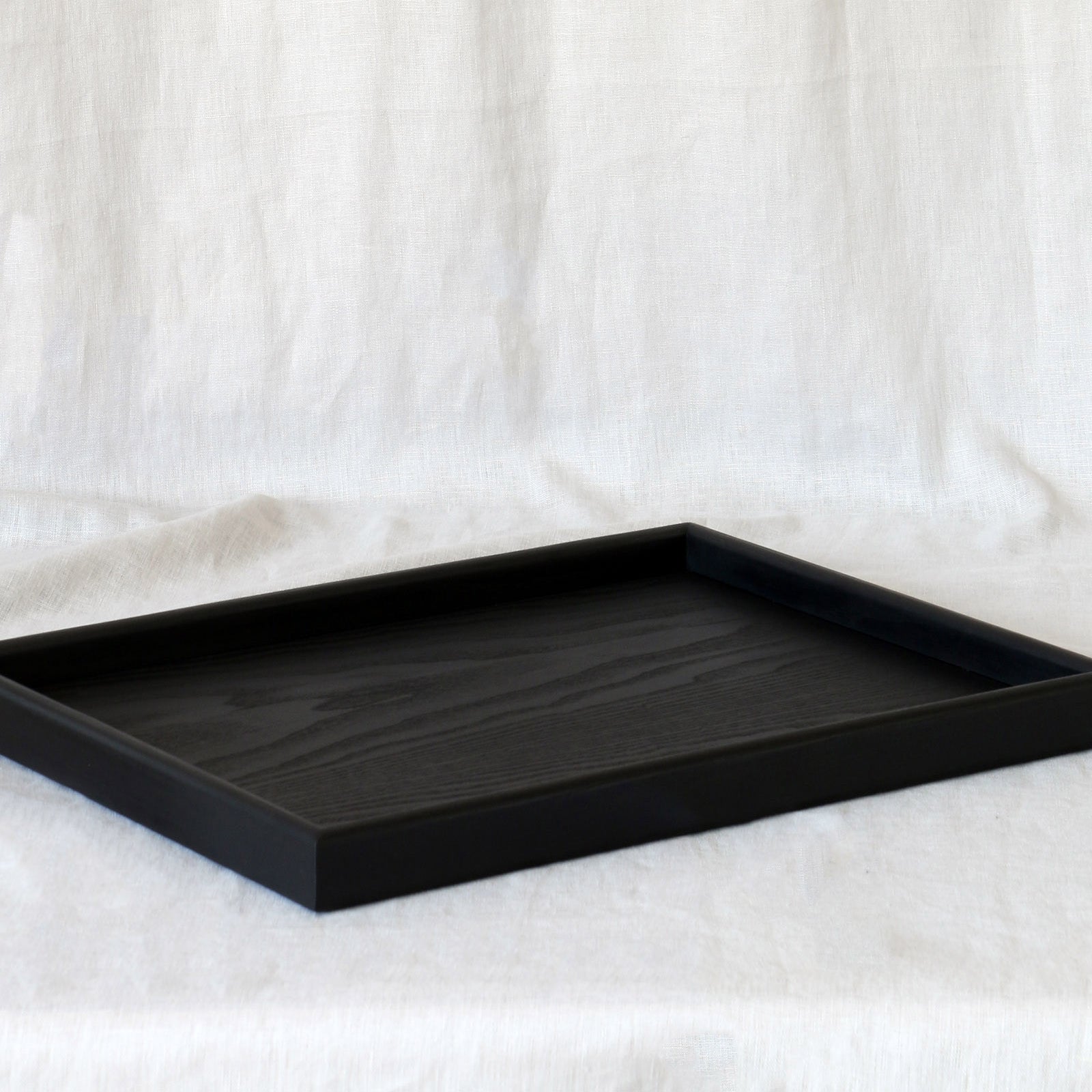 A coffee table tray in black wood, placed on a neutral fabric background, showing its elegant simplicity.