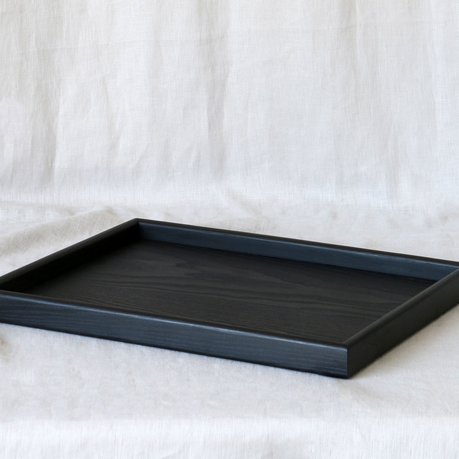 A black wooden tray for footstool, photographed at an angle, highlighting its raised edges and refined construction.